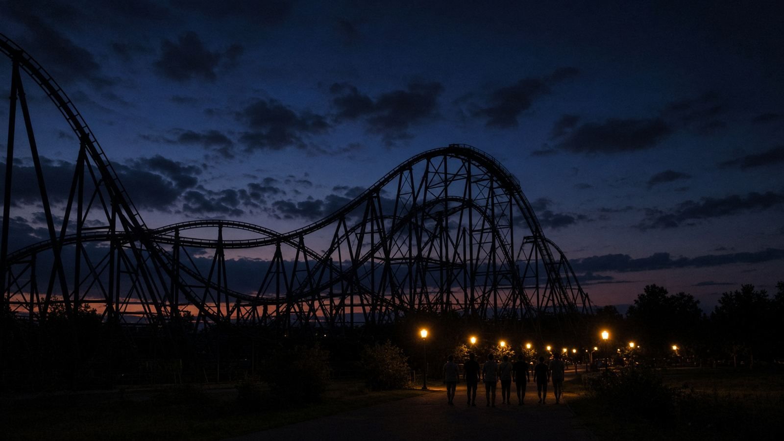A roller coaster against a dusk sky, with path lights along the route below