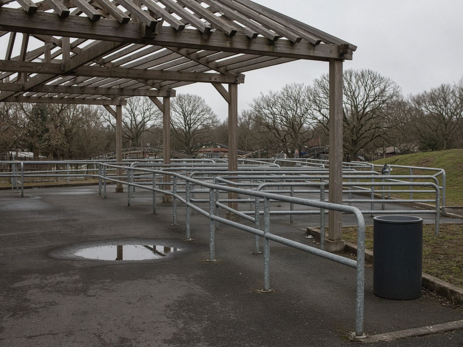 An empty queue shelter with steel rails at a park, on a grey day