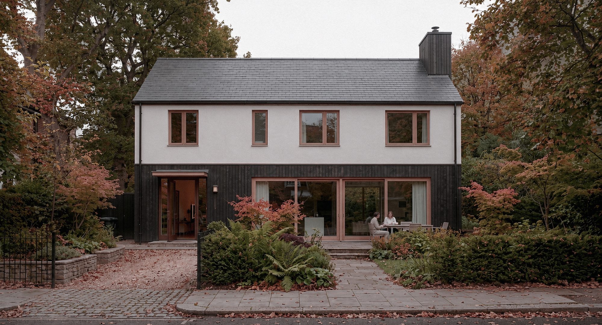 Beech House — a new-build family home with a charred timber ground floor, white lime render above, and coral-pink window and door reveals, set among mature beech and maple in autumn