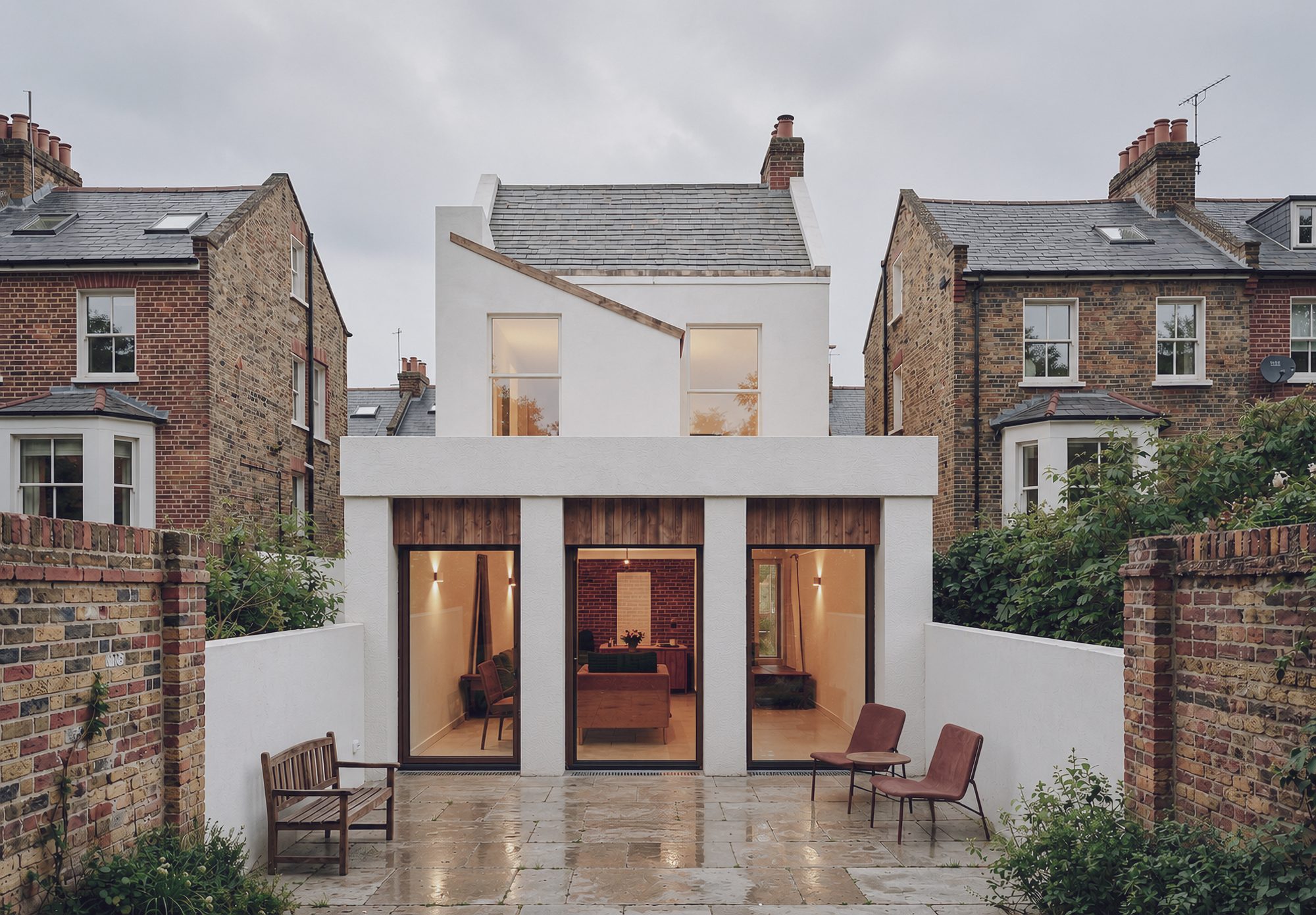 Ashfield House — rear extension with white rendered volume and timber-lined glazed openings at dusk